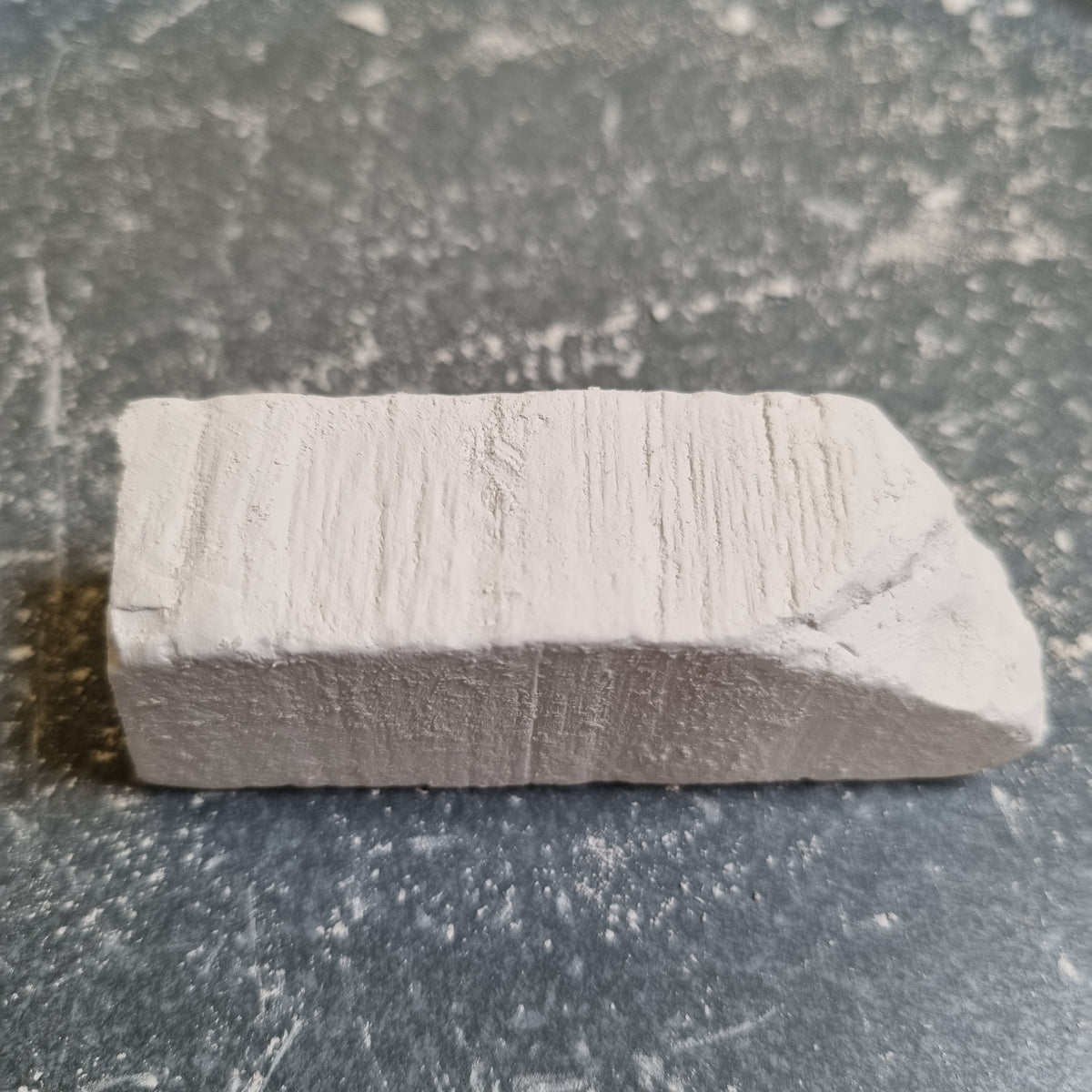 Single rectangular piece of New Oskol white chalk with visible surface grooves on a dark background.