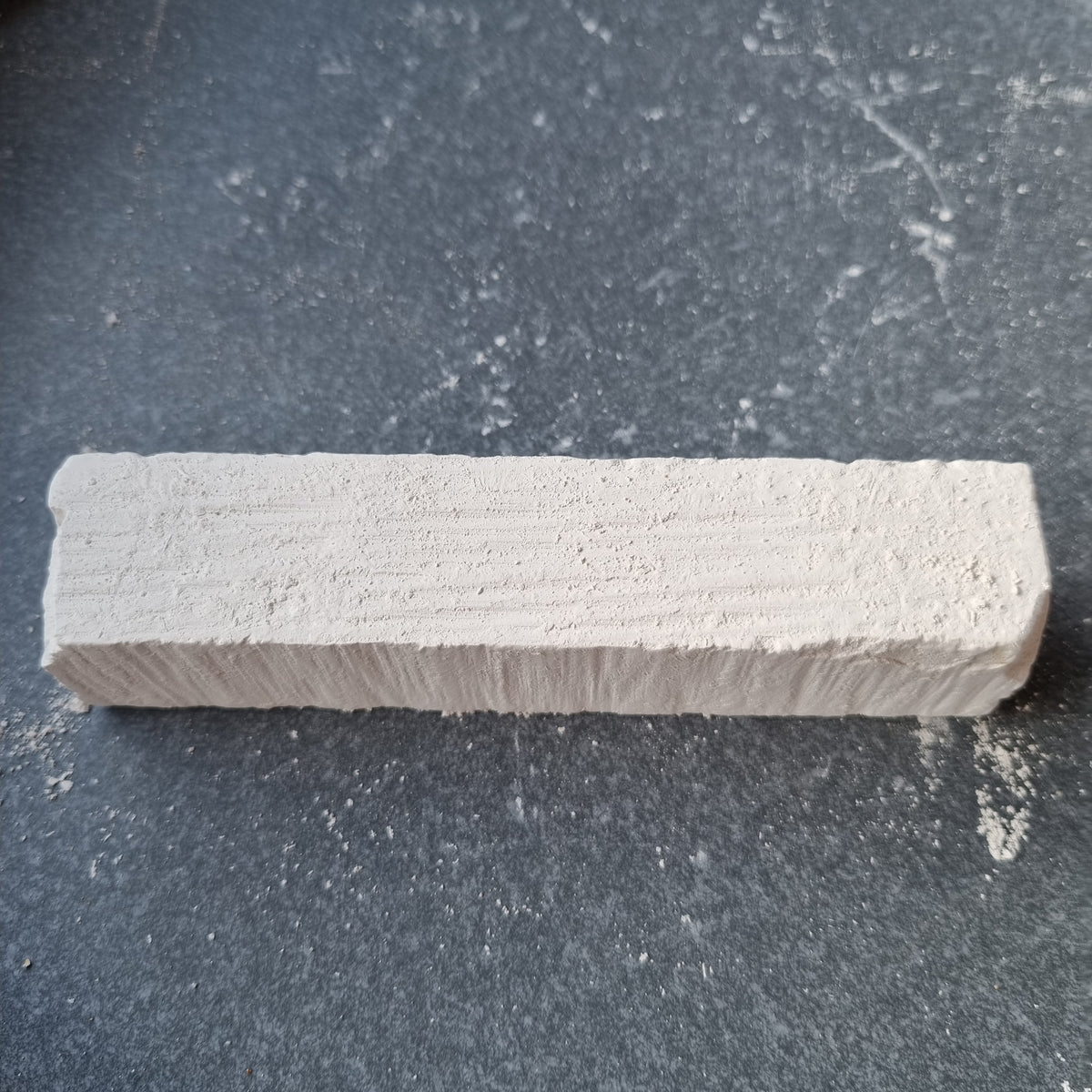 Single rectangular Kristall natural chalk bar viewed at an angle on a dark surface with scattered chalk dust.
