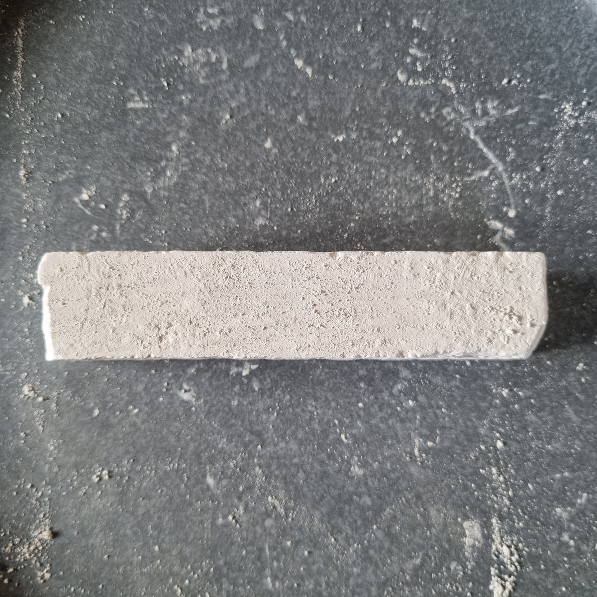 Top view of a white Kristall natural chalk bar with a rough surface, surrounded by chalk dust on a dark background.