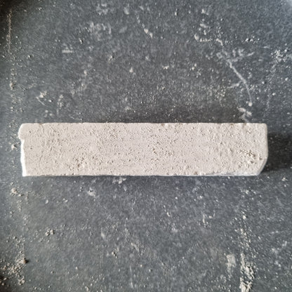 Top view of a white Kristall natural chalk bar with a rough surface, surrounded by chalk dust on a dark background.