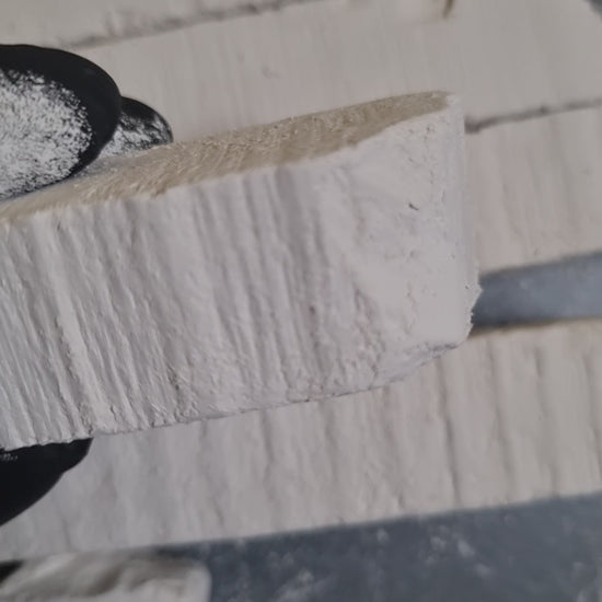 Close-up of New Oskol white chalk with surface grooves, held in a black-gloved hand.